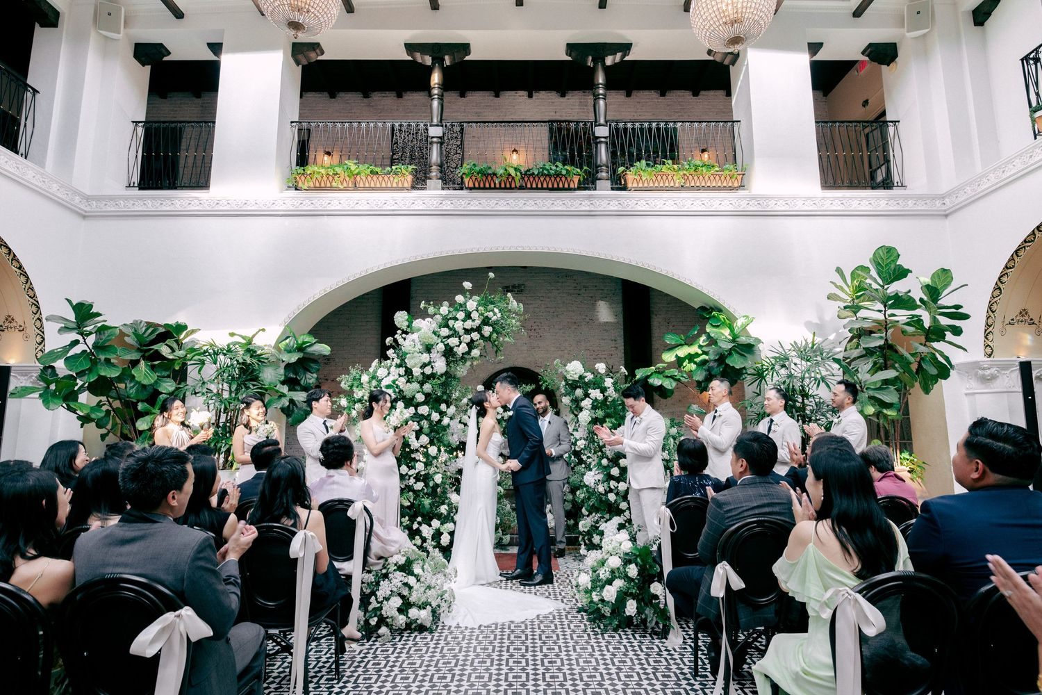 Courtyard ceremony kiss with white florals and guests clapping