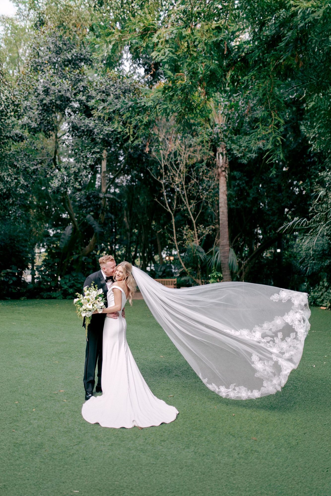 A long lace veil flying across a green lawn