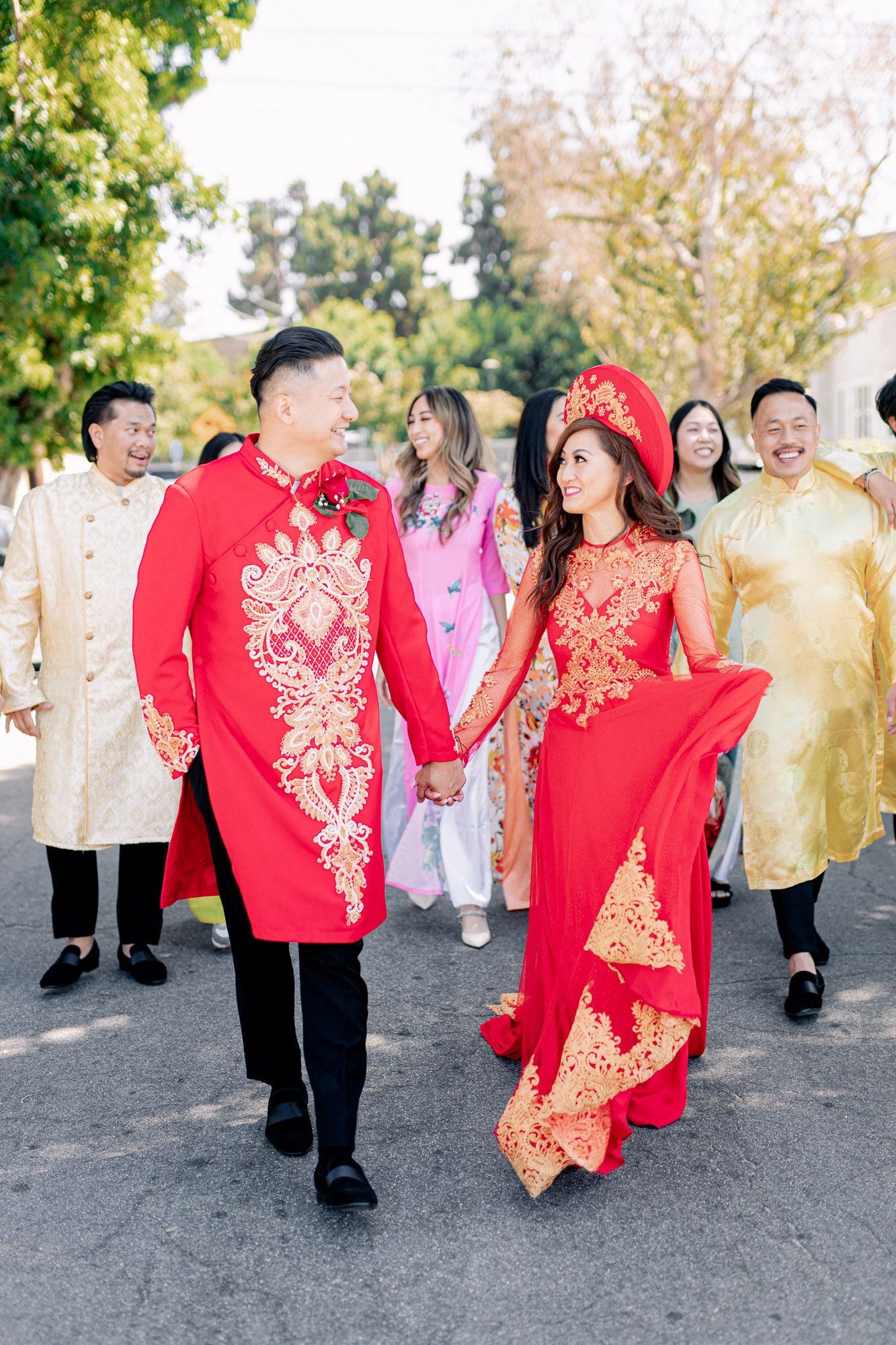 Couple in red áo dài walking with family on the wedding morning